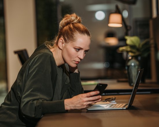 Kvinne som studerer nøye mobil ved pc